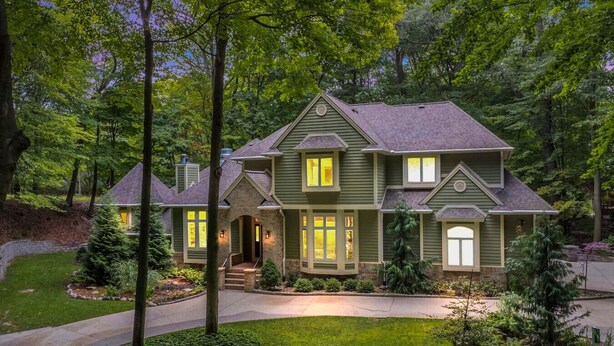 A two-story house with a stone foundation, a wrap-around porch, and a well-maintained front yard with trees and shrubs.