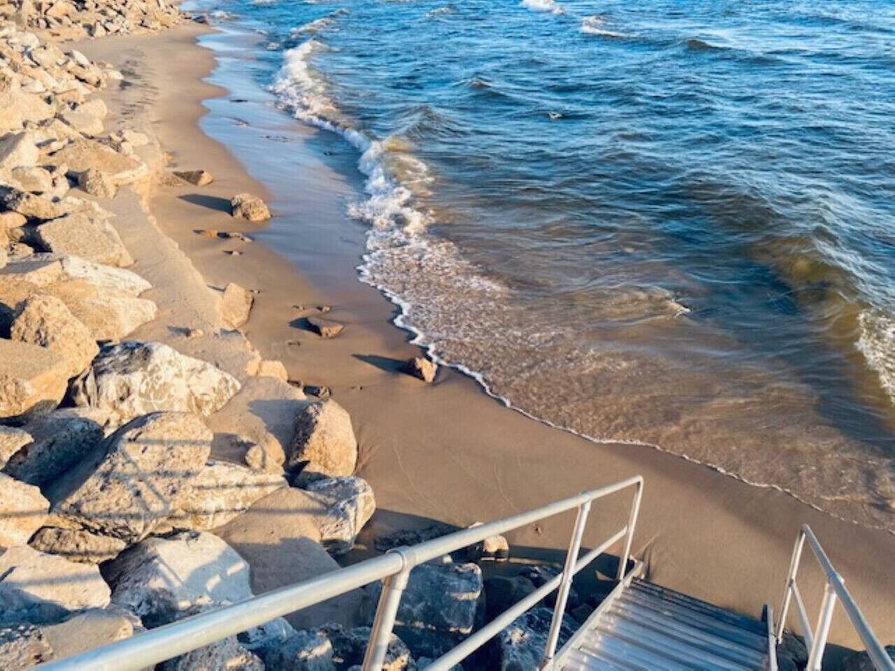 A beach with rocky terrain and a metal staircase leading down to the shore.