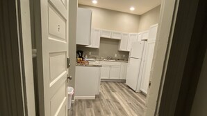 Un pasillo estrecho que conduce a una cocina con armarios blancos, una encimera y un refrigerador.