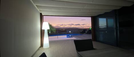 A room with a view of a swimming pool and sunset.