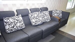 A grey sofa with patterned cushions in a modern room with a striped wall and a tiled floor. - Hotel Pondichery (Puducherry)