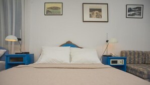 Habitación de hotel con cama, dos mesitas de noche con lámparas, un sofá y tres cuadros enmarcados en la pared.