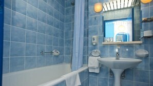 Un baño con azulejos azules, una bañera blanca, un lavamanos y un espejo.