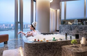 A person relaxing in a hot tub with a city view, a marble countertop with amenities, and a large window. - Conrad Hangzhou (Hangzhou)