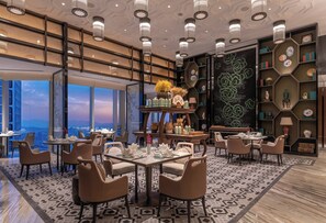 A modern dining area with multiple tables and chairs, a decorative wall with a floral pattern, and a view of the cityscape through large windows. - Conrad Hangzhou (Hangzhou)