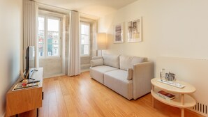 A modern living room with a sofa, a small table with a lamp, and a TV on a wooden desk. - Deluxe Apart with Balcony view to Flores Street (Oporto)