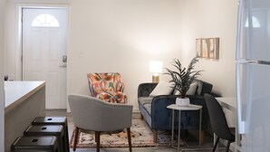 A compact living space with a kitchenette, a sofa, a chair, a small table, and a potted plant.