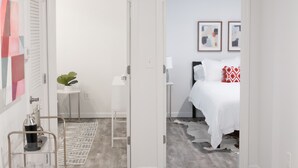 A hotel room with a bed, a small table with a plant, a white radiator, and a patterned rug.