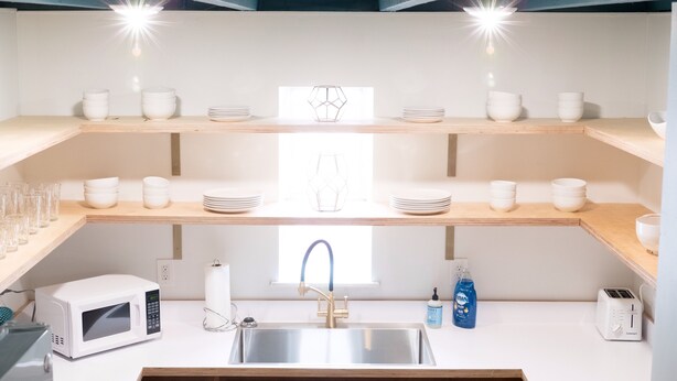 A modern kitchen with a stainless steel sink, a microwave, and a toaster. There are multiple shelves with white bowls and plates.