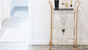 A hallway with a clear glass cart holding a black vase, gold utensils, and crystal glasses.