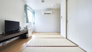 A minimalist living room with a flat-screen TV, a small cabinet, a coffee maker, and a sliding door. - Hotel Select Inn Saitama Moroyama (Moroyama)