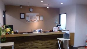 A reception desk with a wooden counter, a clock, framed pictures, and a small plant. - Hotel Select Inn Saitama Moroyama (Moroyama)