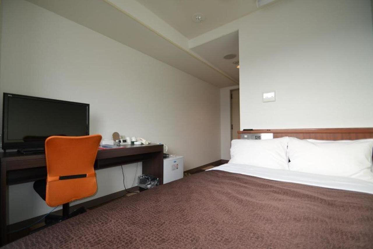 A hotel room with a bed, a desk with a computer, a chair, and a television.