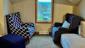 A cozy room with a sloped ceiling, a large window with a view of the outdoors, and two patterned armchairs.