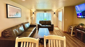 A living room with a sofa, two chairs, a coffee table, a TV, and a framed picture on the wall.