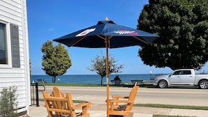 A patio with wooden chairs and a large umbrella, overlooking a body of water.