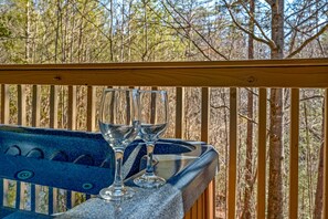 Une terrasse en bois avec une rambarde en verre donnant sur une zone boisée.