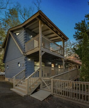 Une cabane à deux étages dotée d’un balcon, d’un escalier et d’une terrasse en bois.