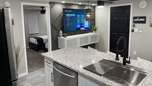 Cozinha moderna com bancada de granito, pia de aço inoxidável e uma televisão de tela plana exibindo serviços de streaming.