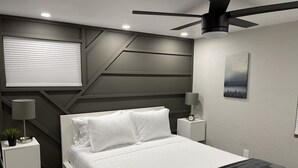 Quarto moderno com cama, mesas de cabeceira, ventoinha no teto, luminária na parede e um quadro.