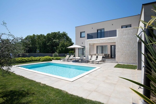 A modern two-story house with a swimming pool, outdoor seating, and a well-maintained garden.