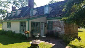 Een huis met twee verdiepingen, een bakstenen schoorsteen, groene sierlijsten en een klein terras met een vuurkorf.