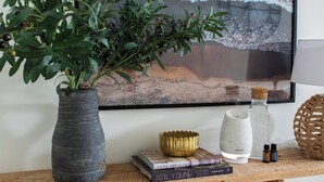 Ein Holztisch mit einem Blumentopf, einem gerahmten Bild, einer Flasche und einem Buch.
