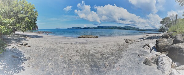 Une plage avec un ciel dégagé, une eau calme et des montagnes à l’horizon.