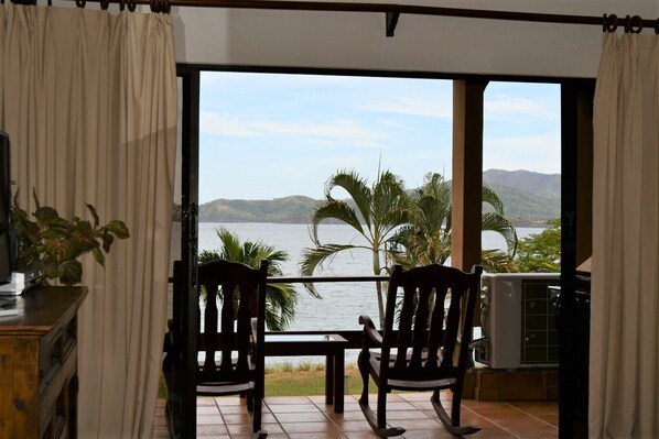 A room with a view of a lake and mountains, featuring two rocking chairs and a table.