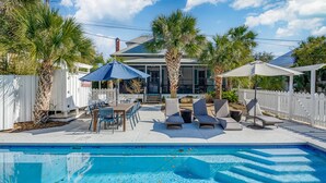 A backyard with a swimming pool, lounge chairs, a table, and umbrellas.