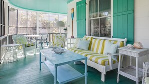 A covered porch with a white sofa, striped cushions, and a table with a decorative bowl.