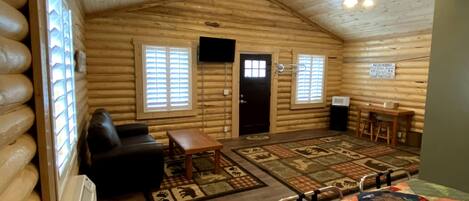 Ein Blockhaus-Interieur mit einer gemütlichen Wohnbereitschaft, einem Kamin, einem großen Bett und einem Esstisch.