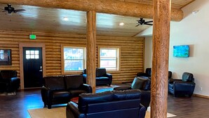 A spacious lobby with wooden walls and floors, leather sofas, a chandelier, and a television on the wall. - Cabin Village (Island Park)