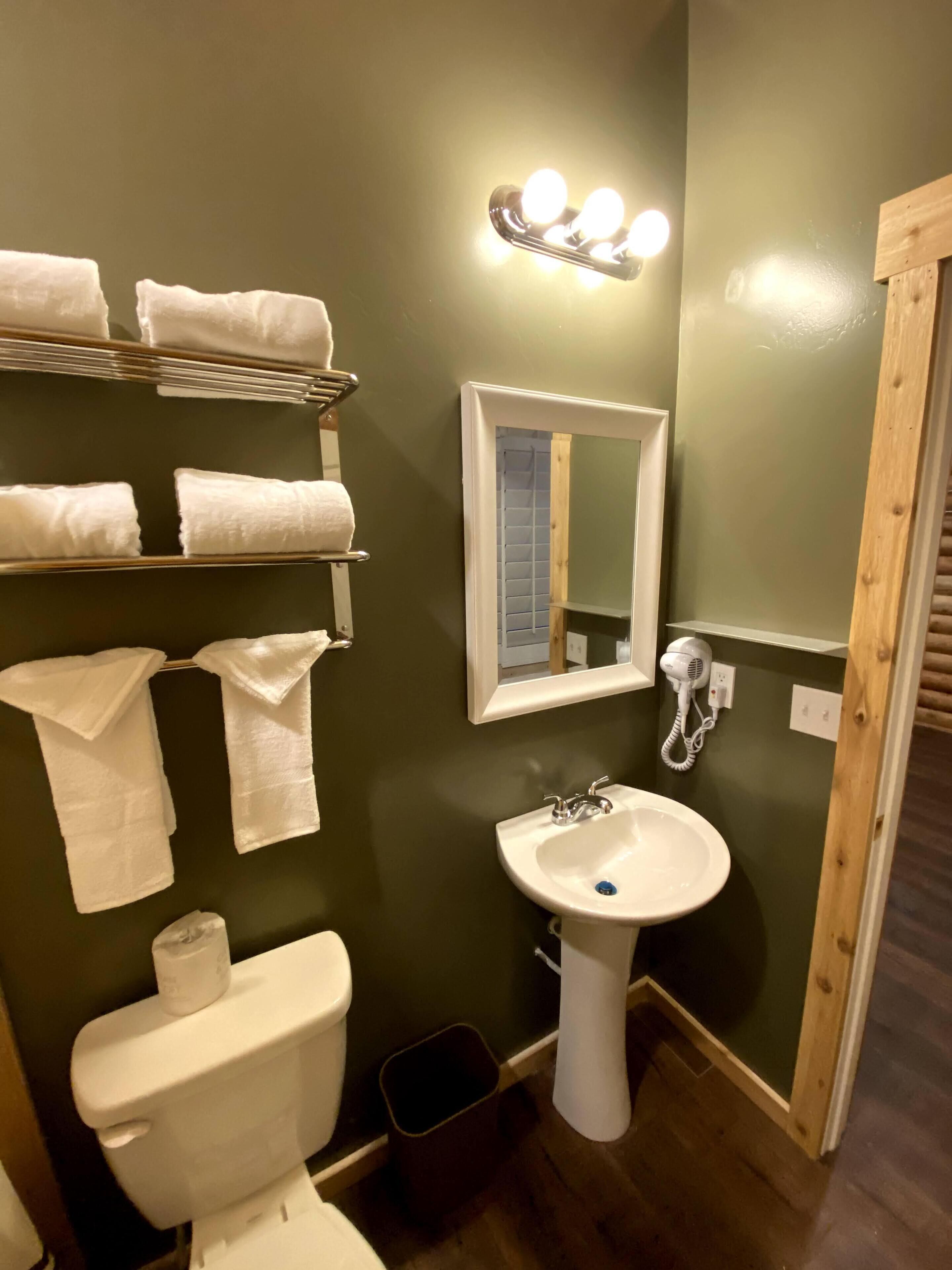 A bathroom with a white sink, a mirror, a towel rack with towels, a toilet, and a hairdryer on the wall.