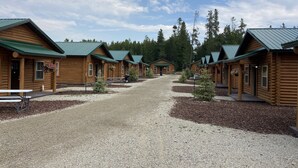 A row of log cabins with green roofs, arranged in a line with gravel paths in between. - Cabin Village (Island Park)
