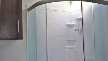 A shower with a curved glass door, white tiles, and a wooden cabinet to the left.