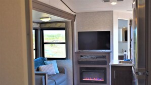 En kompakt autocamper-indretning med sofa, fjernsyn, brændeovn og et lille tekøkken.
