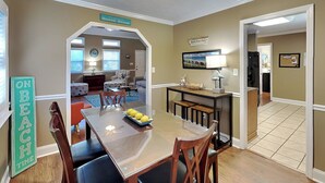 Een eethoek met een tafel en stoelen, een keuken achtergrond en een bord met de tekst 'Welcome to our Beach House'.