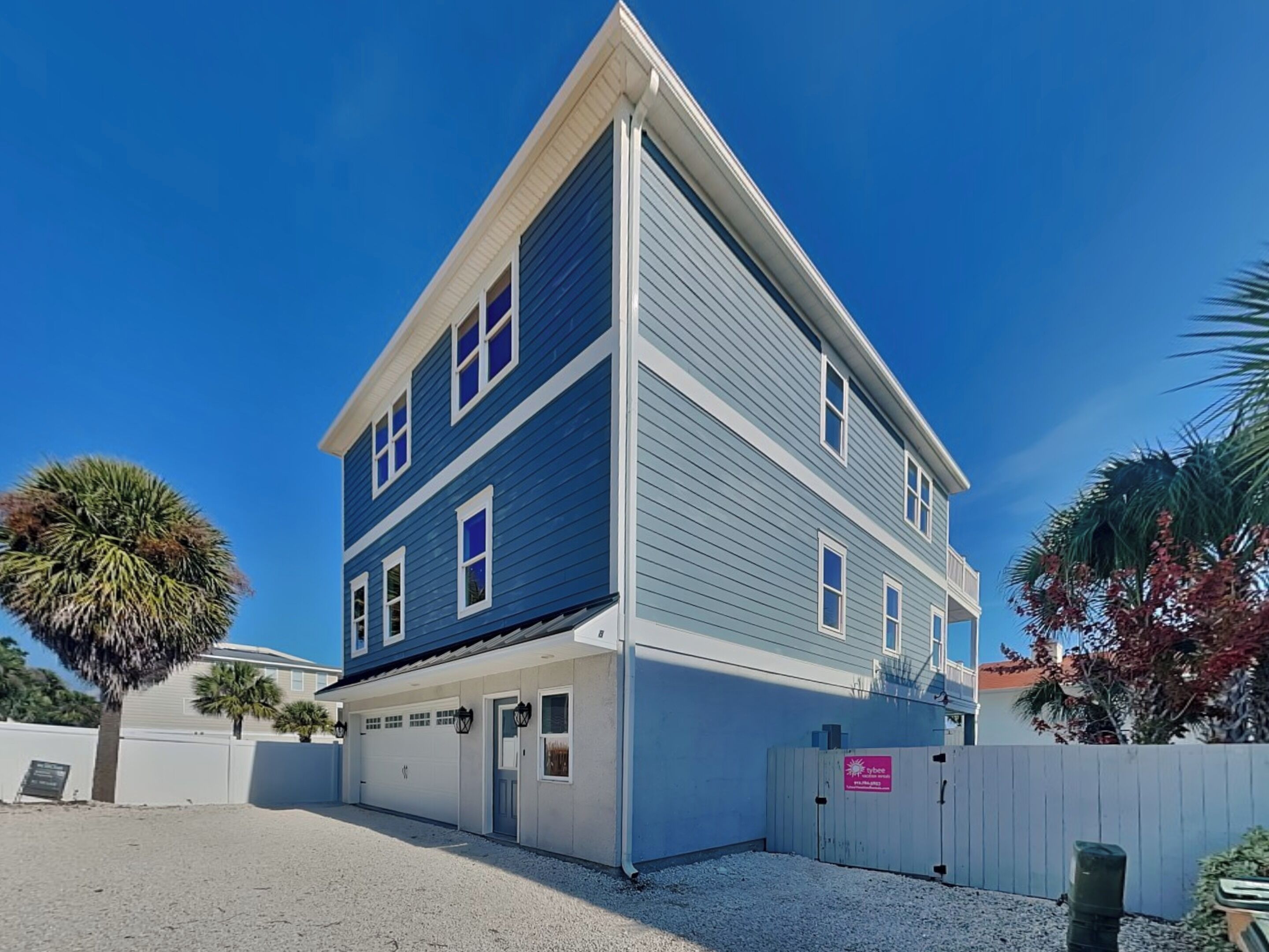 A two-story building with a garage, a covered driveway, and a white fence.