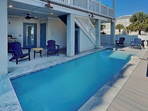 Una piscina con agua azul, rodeada por una terraza de madera y sillas Adirondack azules.