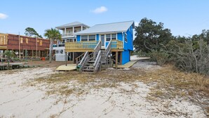 A beachfront house with a wooden deck and stairs leading to a balcony.