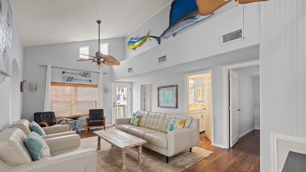 A spacious living room with a white leather sofa, a wooden coffee table, and a ceiling fan.
