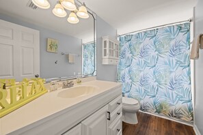A bathroom with a white vanity, a sink, a mirror, and a toilet. There is a shower curtain with a leaf pattern. - Bayfront Vacation Home! (Gulf Shores)