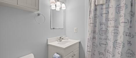 A bathroom with a white sink, mirror, and cabinet, a towel hanging on the wall, and a shower curtain with positive phrases.