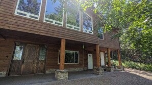 A two-story wooden house with a covered porch, large windows, and stone pillars. - Hanging Rock Get Away (Bigfork)