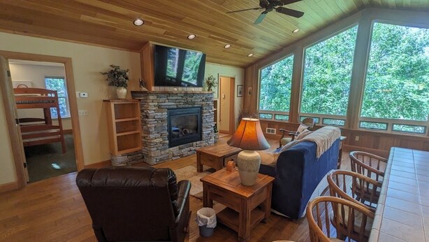 A cozy living room with a stone fireplace, comfortable seating, and large windows offering a view of the outdoors. - Hanging Rock Get Away (Bigfork)