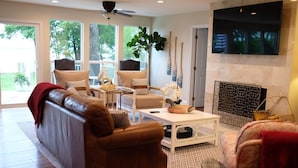 A living room with a brown leather sofa, two armchairs, a coffee table, and a fireplace. - Modern Lakefront Cottage on Open Water with Stunning Sunsets on Cedar Creek Lake (Trinidad)