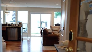 A spacious living area with a wooden floor, a sofa, a dining table, and a kitchen area with a dishwasher. - Modern Lakefront Cottage on Open Water with Stunning Sunsets on Cedar Creek Lake (Trinidad)