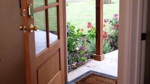 A wooden door with a glass panel, leading to a garden with a bench and a doormat. - Modern Lakefront Cottage on Open Water with Stunning Sunsets on Cedar Creek Lake (Trinidad)