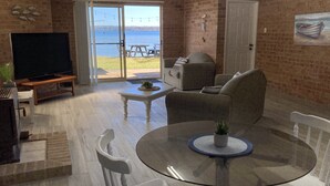 Een woonkamer met een glazen tafel, witte stoelen, een bank en een televisie.